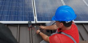 Monteur mit Messgerät vor einem Solarmodul auf dem Dach.