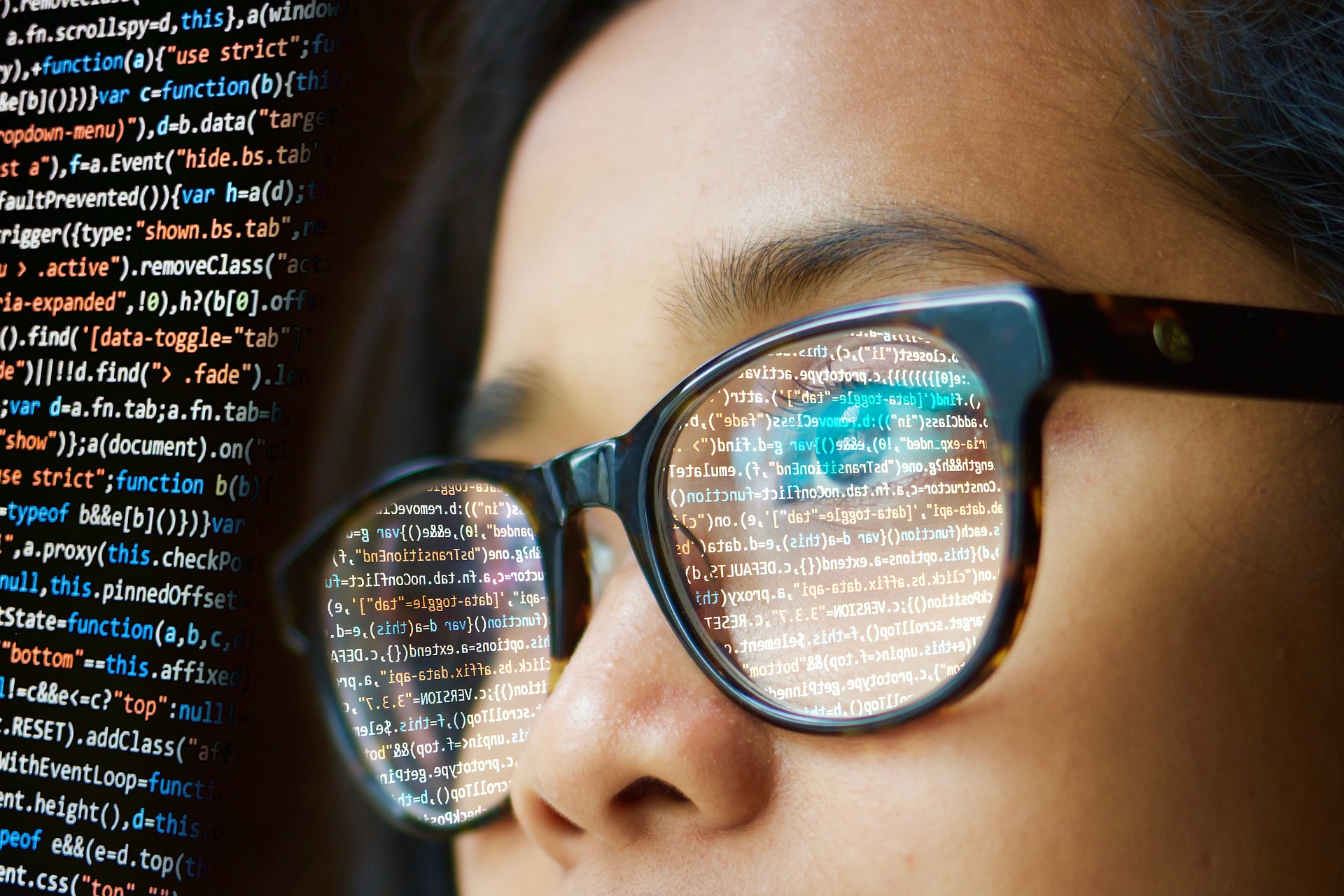 Frau mit Brille schaut auf einen Computerbildschirm mit Programmiersprache.