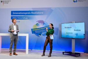 Preisverleihung Innovationspreis Reallabore 2020 mit Moderatorin und Moderator auf der Bühne.