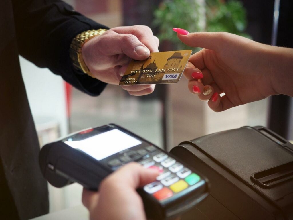 Kund reicht Kreditkarte zum Bezahlen an Kassierer mit Terminal in der Hand.