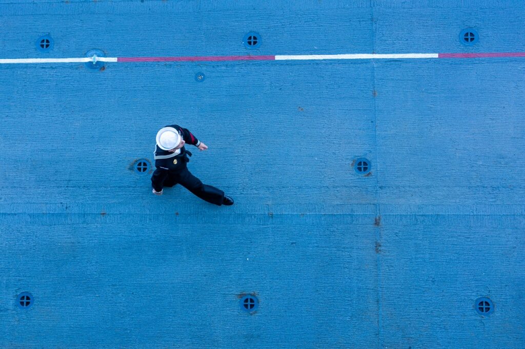 Vogelperspektive auf einen Marinesoldaten, der über das Deck eines Schiffes geht.