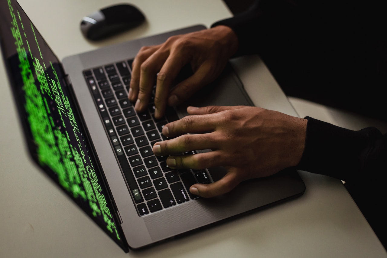 Eine Person sitzt vor einem Laptop mit Code auf dem Bildschirm und tippt auf der Tastatur.