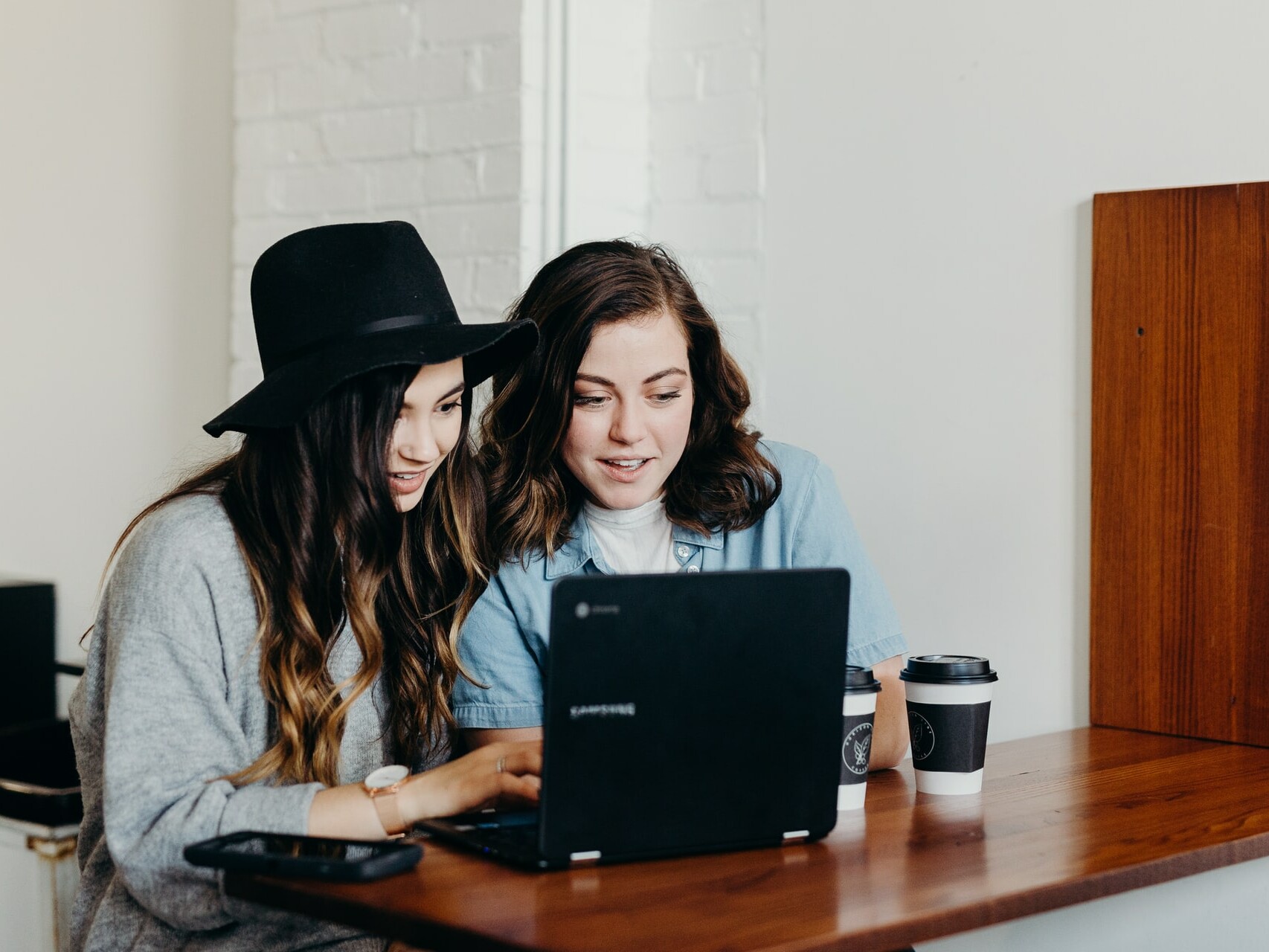 Zwei junge Frauen sitzen vor dem Laptop und shoppen onlien.