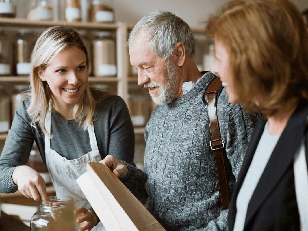 Ein älteres Paar lässt sich in einem Geschäft von einer jüngeren Frau beraten.