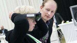 Eine Person setzt sich eine VR-Brille auf, eine andere schaut zu.