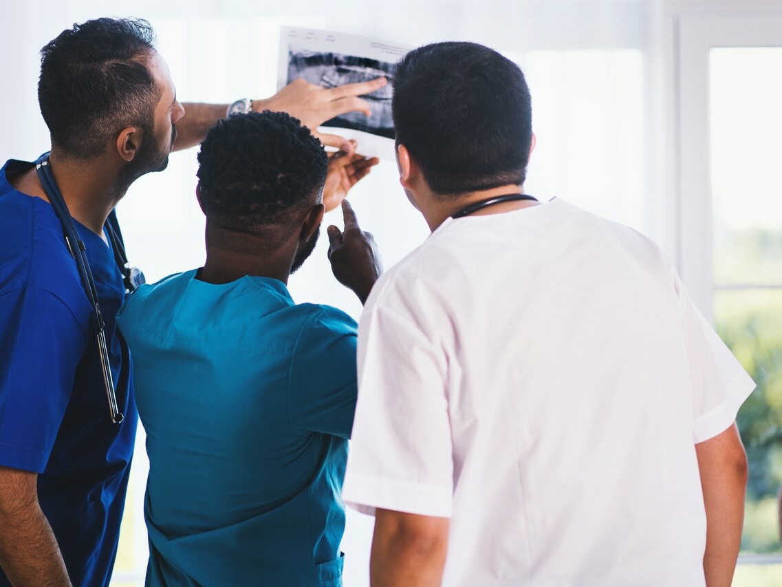 Drei Mediziner stehen mit dem Rücken zur Kamera und betrachten ein Röntgenbild.