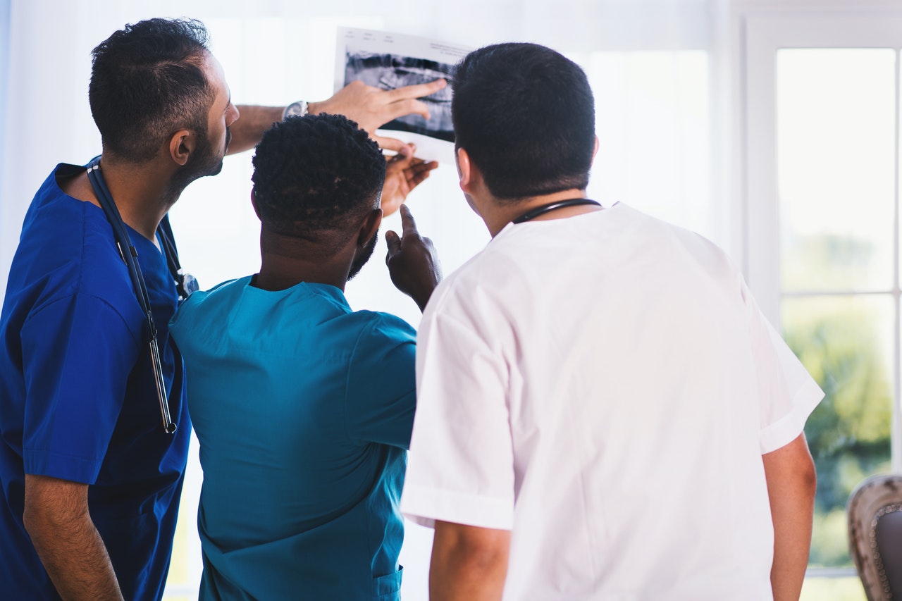Drei Mediziner stehen mit dem Rücken zur Kamera und betrachten ein Röntgenbild.