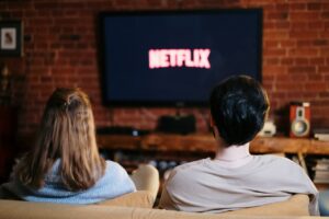 Eine Frau und ein Mann sitzen auf dem Sofa vor einem Fernseher mit Netflix-Logo.