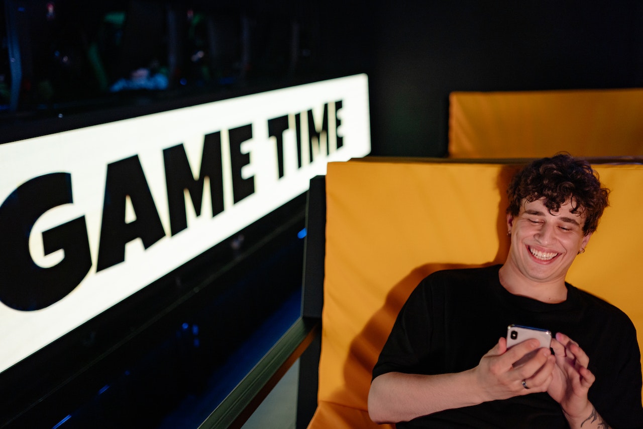 Ein junger Mann sitzt lächelnd auf einem Sessel und spielt mit dem Smartphone.