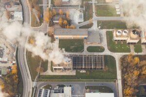 Luftbild einer Fabrik, aus deren Schornstein weißer Rauch aufsteigt.