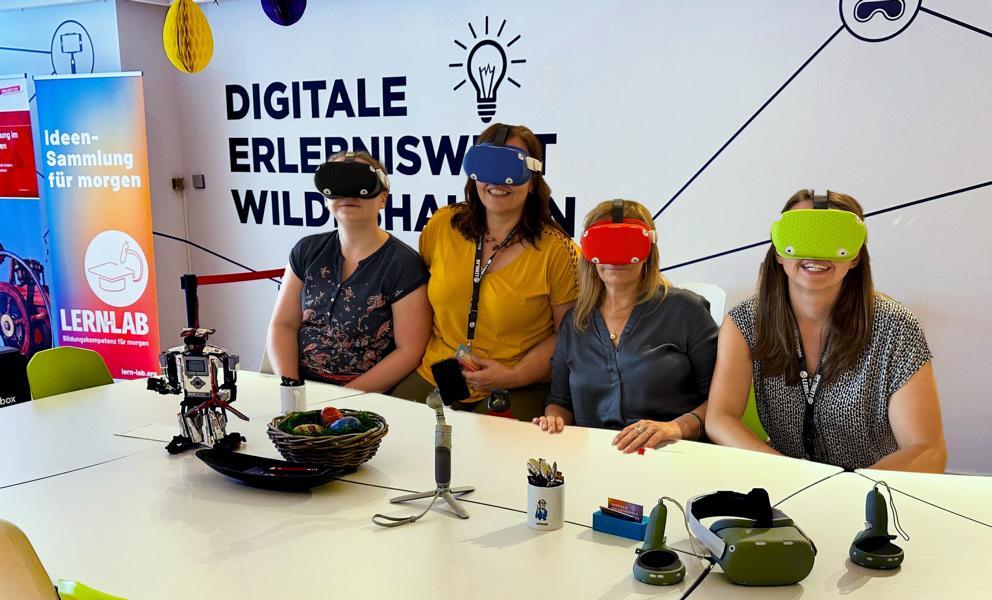 Vier Frauen mit bunten VR-Brillen sitzen an einem Tisch.