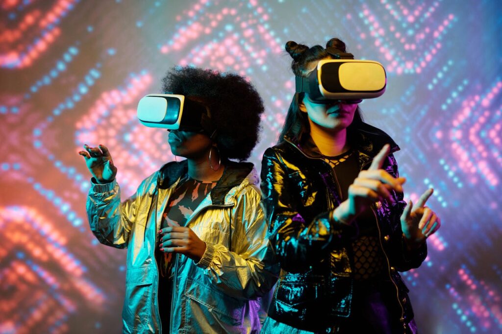 Zwei Frauen mit VR-Brillen agieren vor einem bunt beleuchteten Hintergrund.