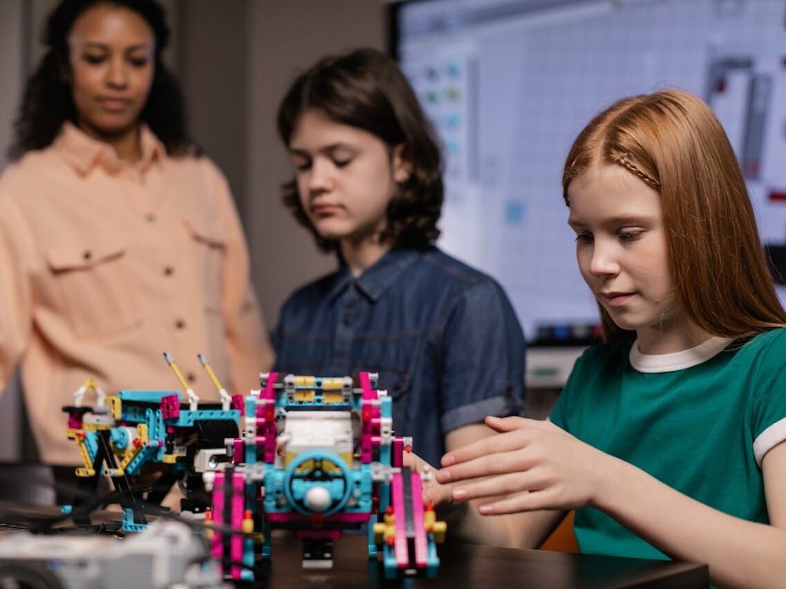 Lehrerin mit Junge und Mädchen im Klassenraum mit Robotik-Modellen.