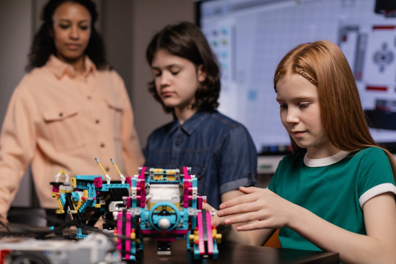 Lehrerin mit Junge und Mädchen im Klassenraum mit Robotik-Modellen.
