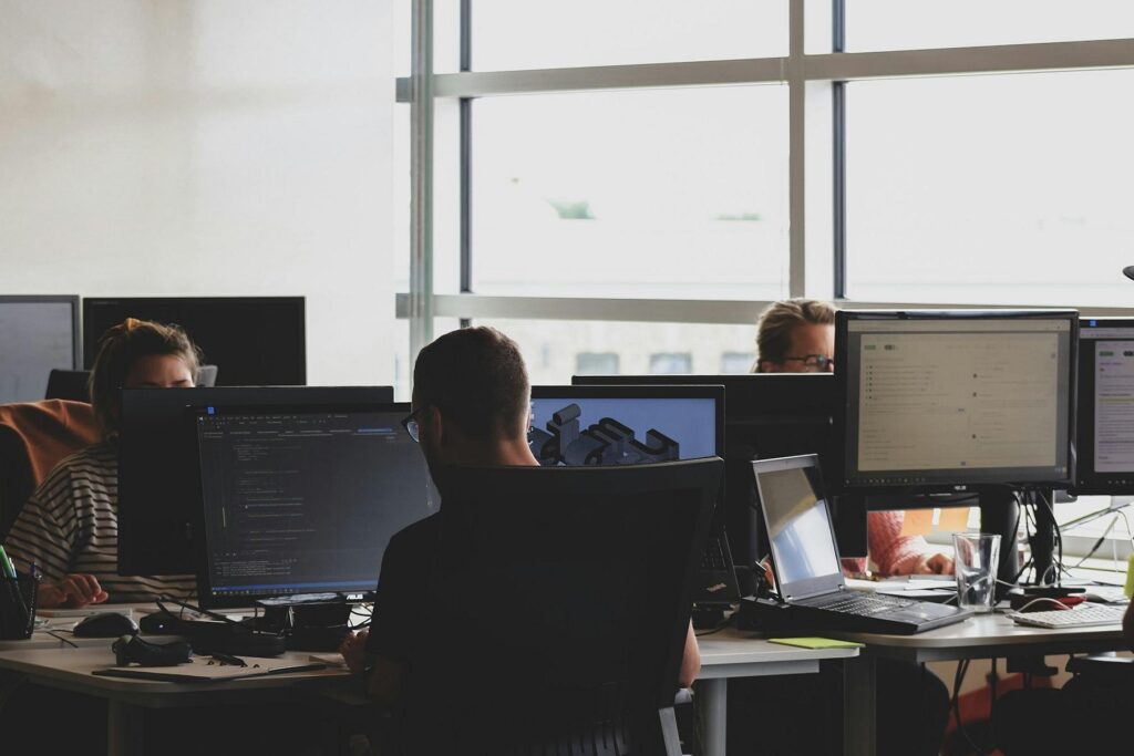 Blick in ein Großraumbüro mit drei Personen vor Computern.